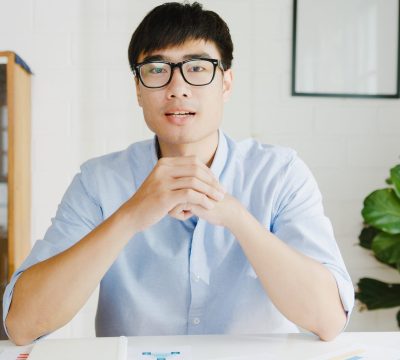 Young Asia businessman using computer laptop talk to colleagues about plan in video call meeting while working from home at living room. Self-isolation, social distancing, quarantine for corona virus.